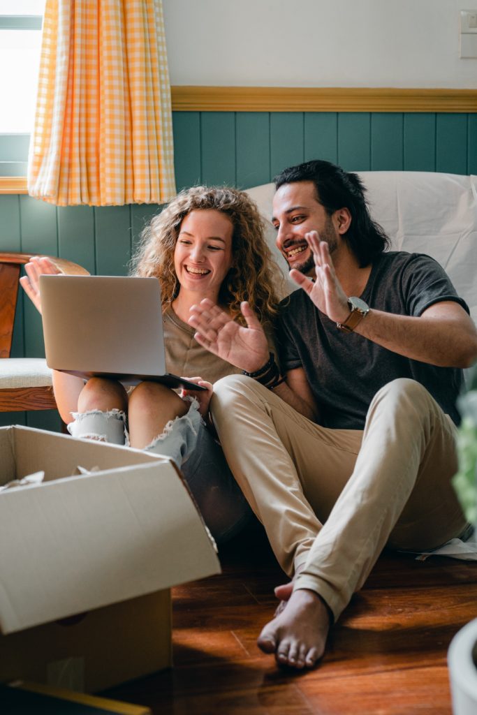 a man and a woman waving in front of a laptop