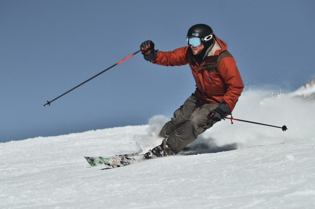 A man in a red jacket and grey pants skiing. 